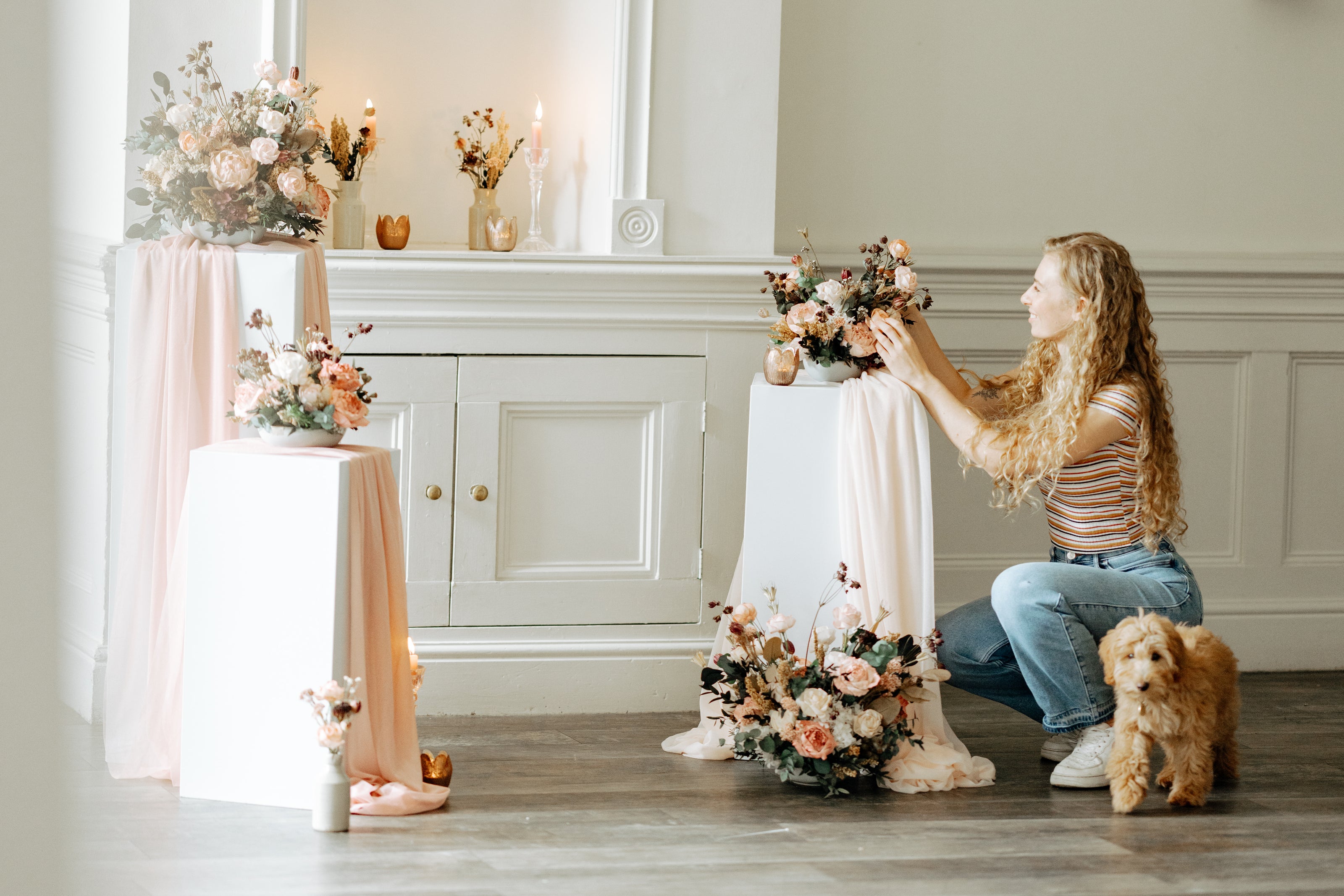 Woman arranging flowers in a room with decorative elements and a dog.