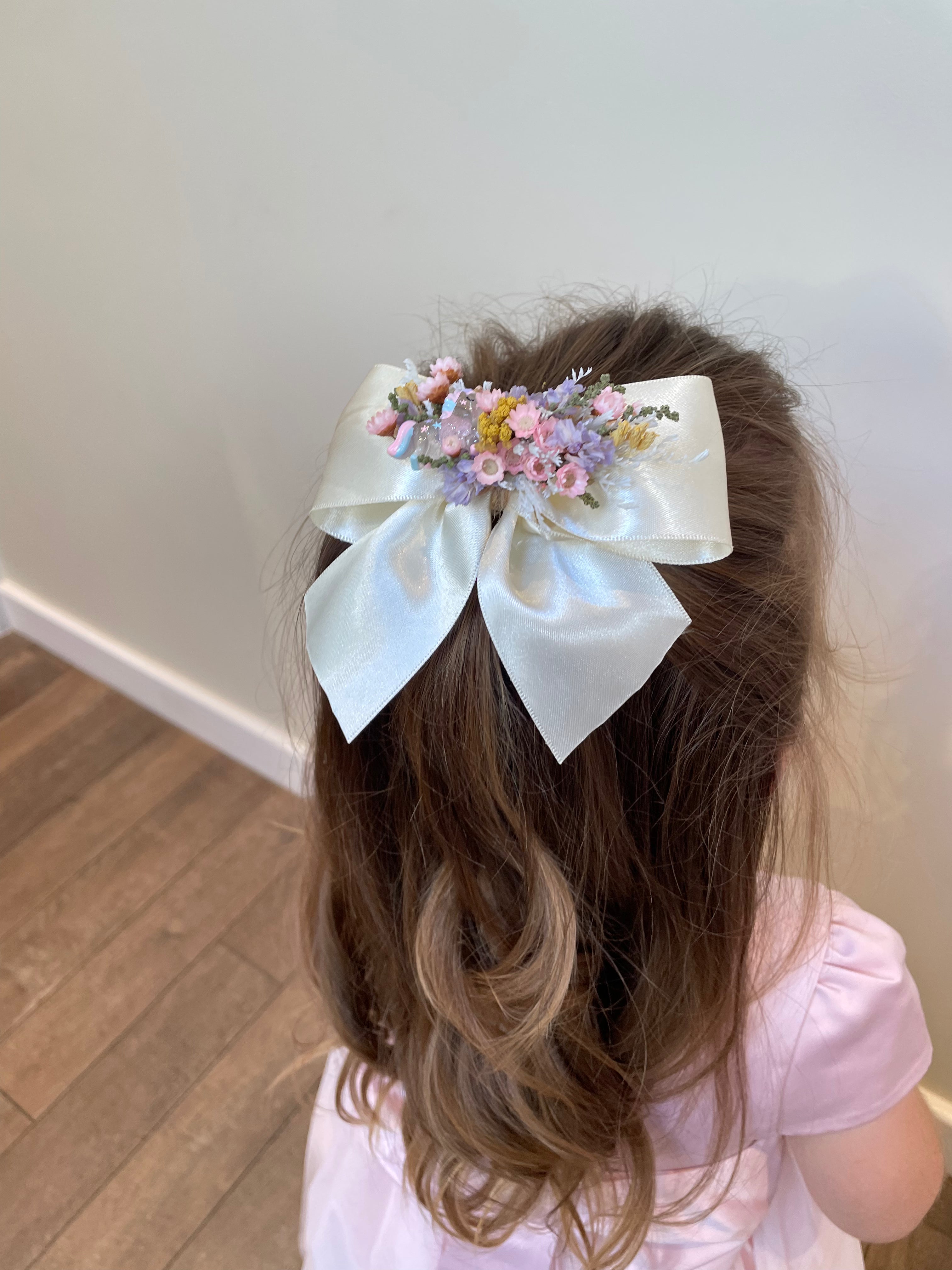 Child with a large bow hair clip decorated with dried flowers in pastel colours. hair clip was handmade in Derbyshire